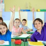 School children raising hands in classroom.